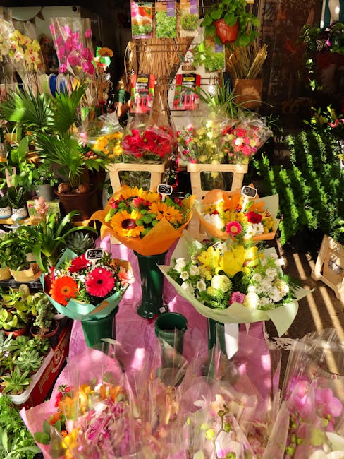 A vibrant display of fresh floral bouquets arranged on a pink cloth-covered table inside a flower shop. The bouquets feature bright colours including pink, yellow, white, and orange, with flowers such
